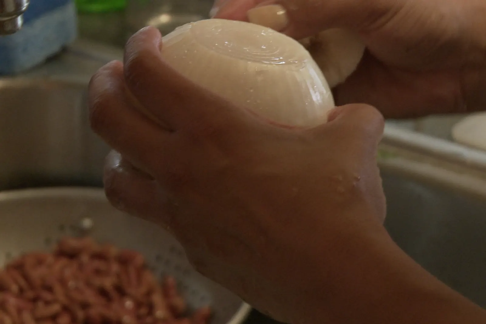 Hands rinsing an onion at the kitchen sink